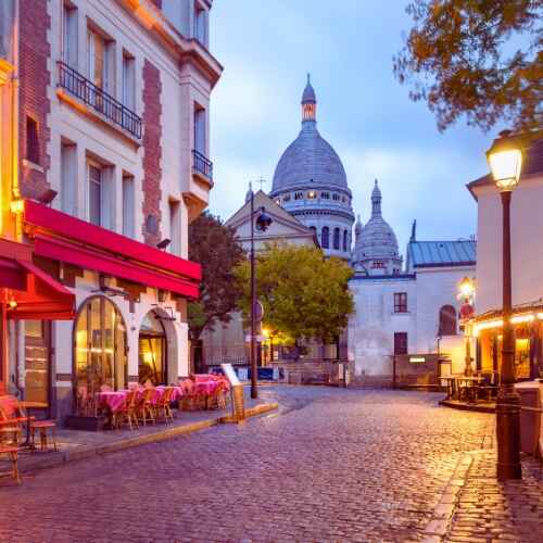 Paris 48 Hours Guide – charming cobblestone street in Montmartre with cozy café tables and a stunning view of Sacré-Cœur at sunrise.