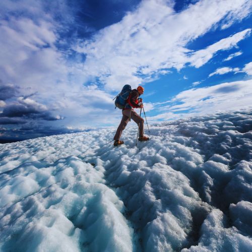 Iceland glacier hiking guide showing a hiker with backpack and poles walking across bright blue ice under a dramatic sky.