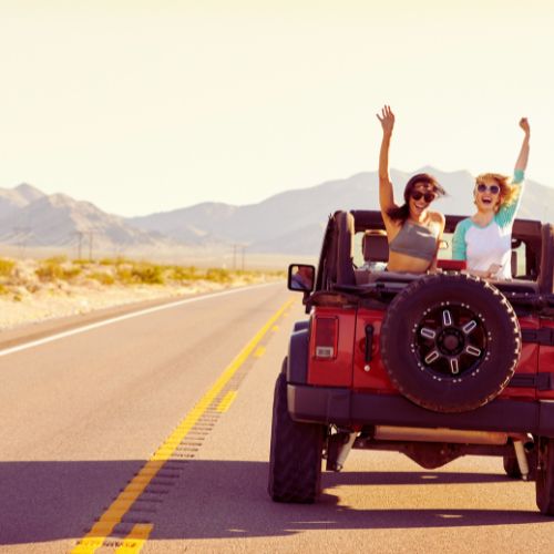 Female travelers practicing zero-waste travel packing on a road trip adventure in a red jeep through desert mountains.