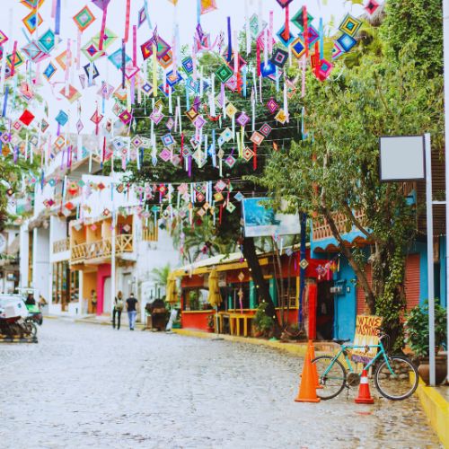 Colorful street decorations hanging above a cobblestone road in Mexico with cafes and bicycles
